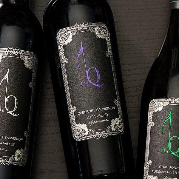 Three elegant wine bottles on dark surface.
